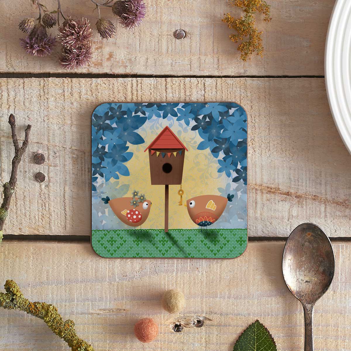 square coaster with illustration of two birdies at their new birdhouse home