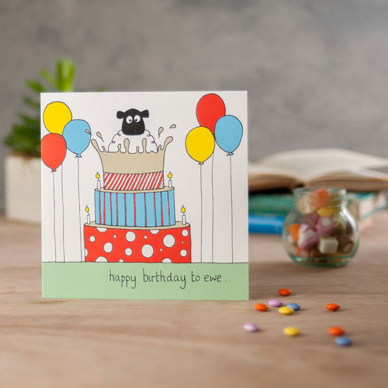 Square card with an illustration of a sheep popping out of a cake and the words happy birthday to ewe