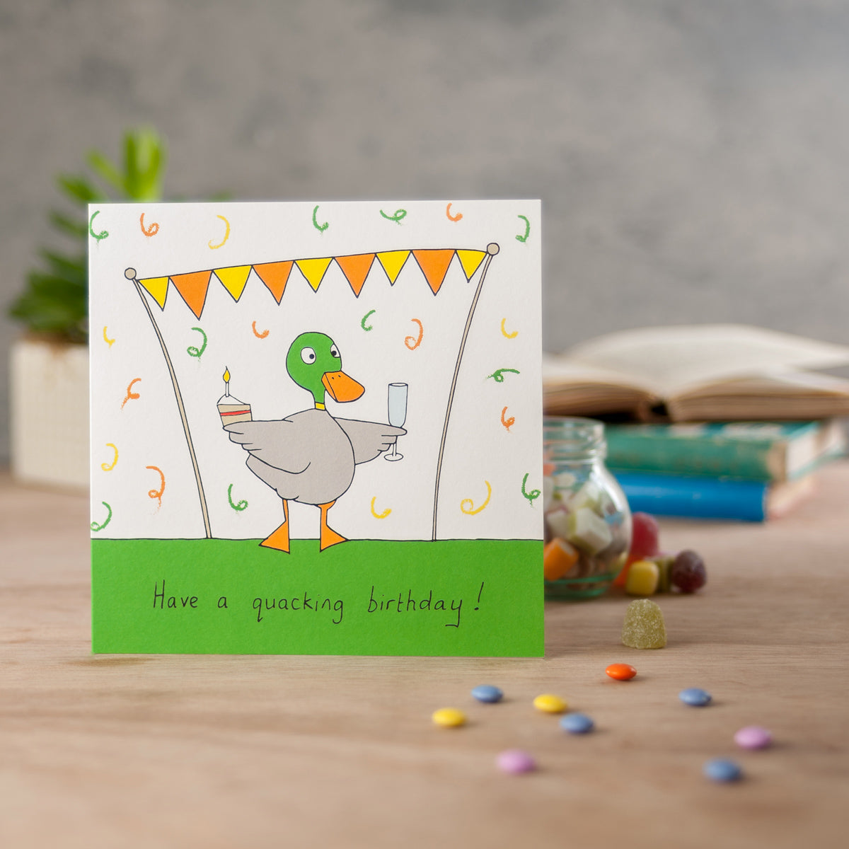 Square card with a duck holding a drink and cake and the words have a quacking birthday