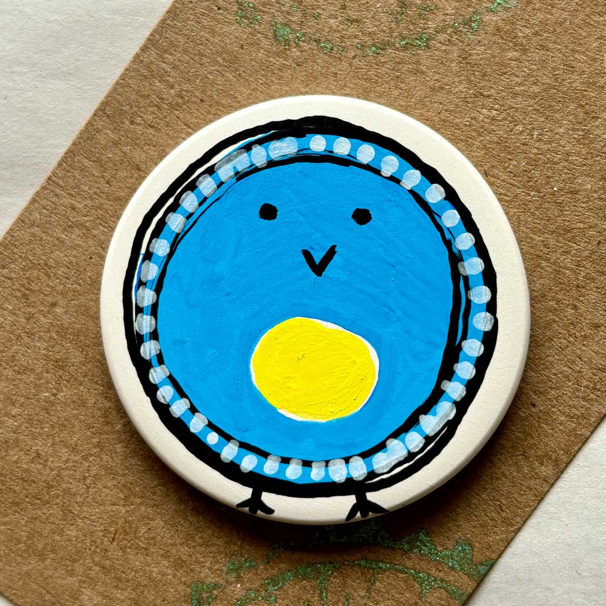 circular ceramic brooch with a hand painted blue tit blob bird illustration