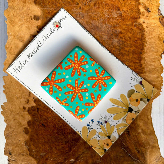 square ceramic brooch with orange and turquoise floral pattern
