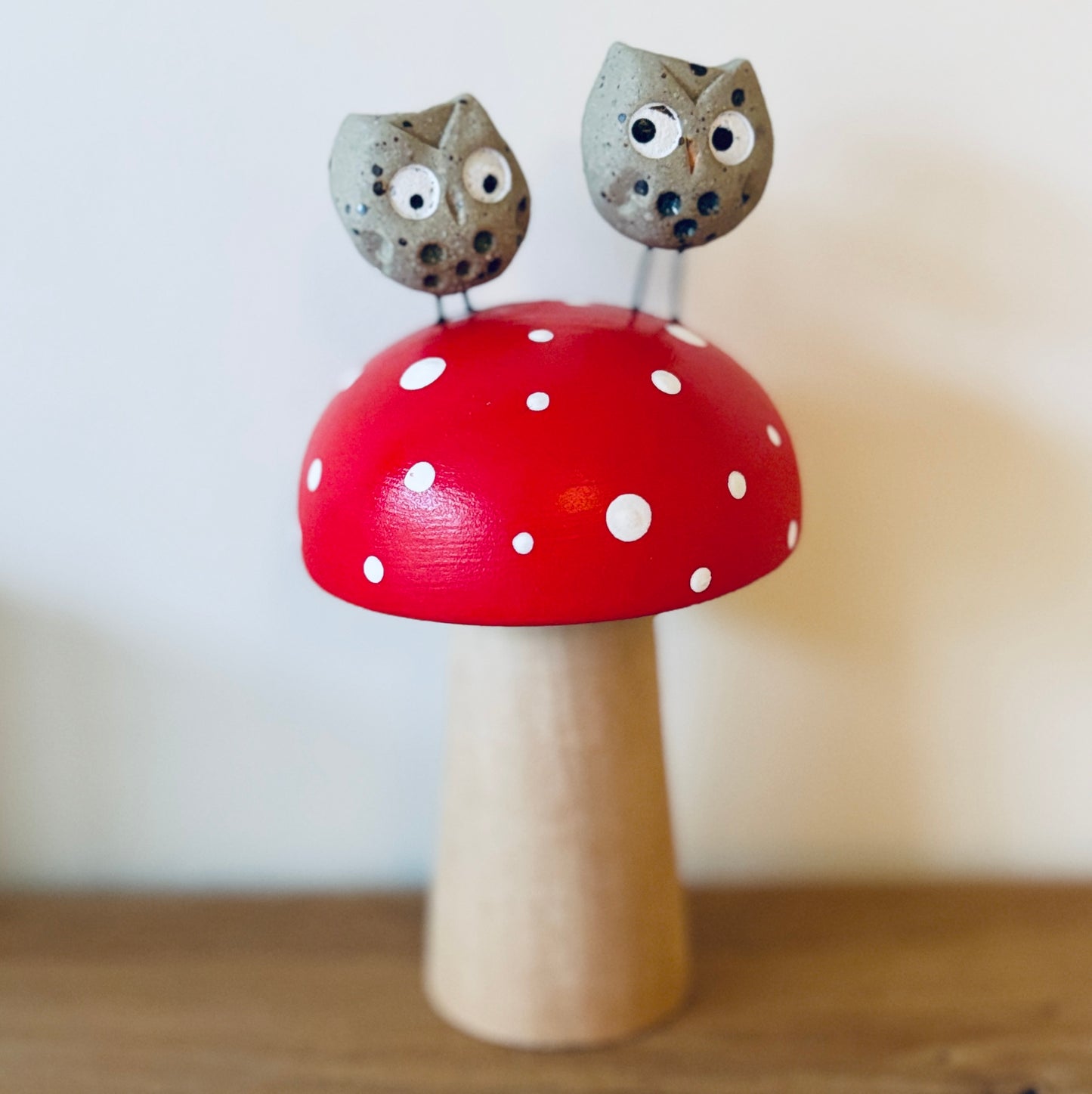 A couple of owls sat on a hand painted wooden toadstool. One of them looks cross and the other sheepish