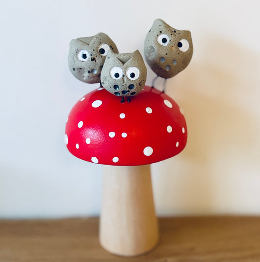 A little family of three clay owls sat on a hand painted wooden toadstool