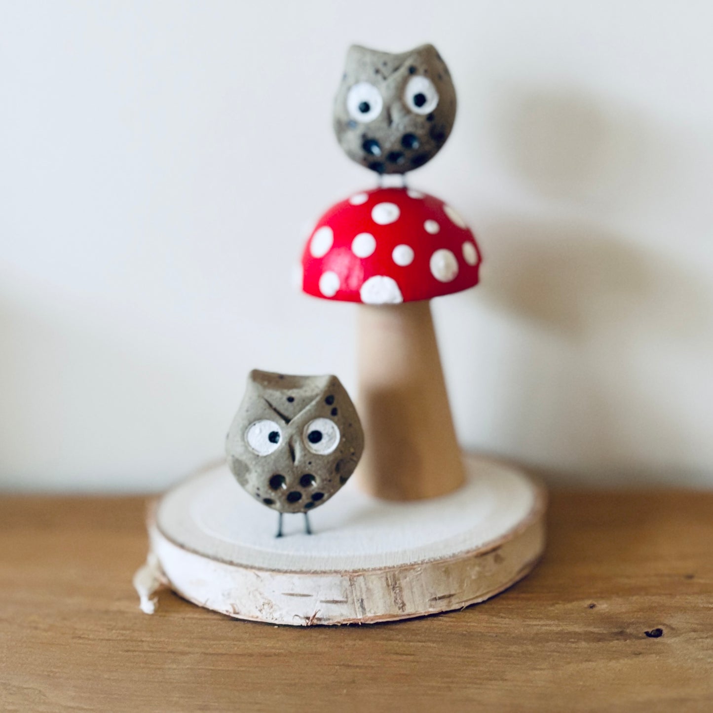 A slice of wood with a hand painted wooden toadstool and two tiny ceramic owls