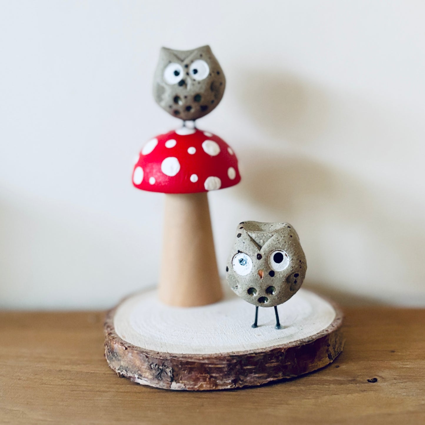 A slice of wood with a hand painted wooden toadstool and two tiny ceramic owls