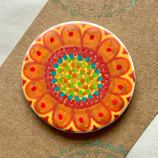 circular ceramic brooch with warm coloured doodle of a sunflower