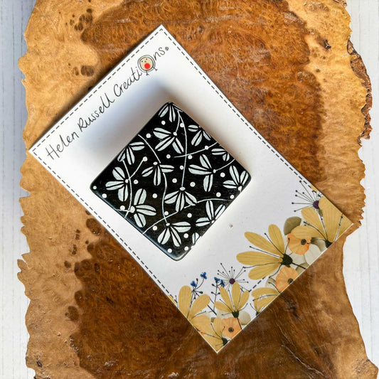 square ceramic brooch hand painted with a black and white design inspired by Japanese fans