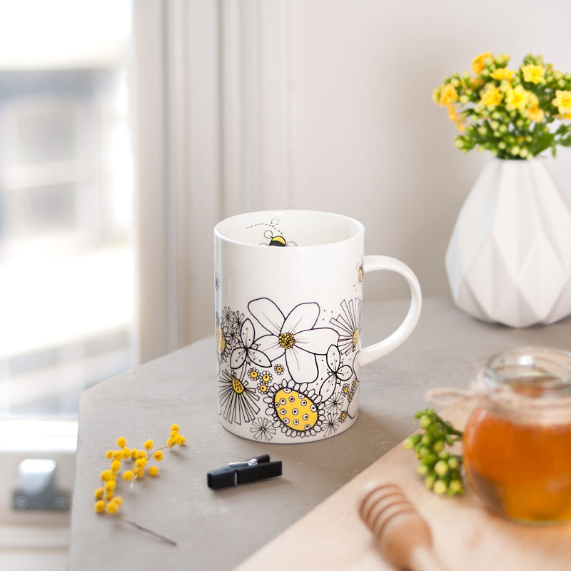 Mug with floral design on a table with a vase and flowers
