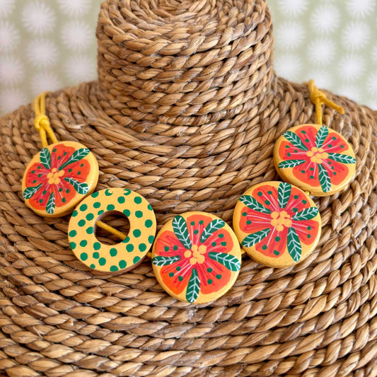 flat circular beads hand painted with tropical flowers and then threaded on bright yellow cord