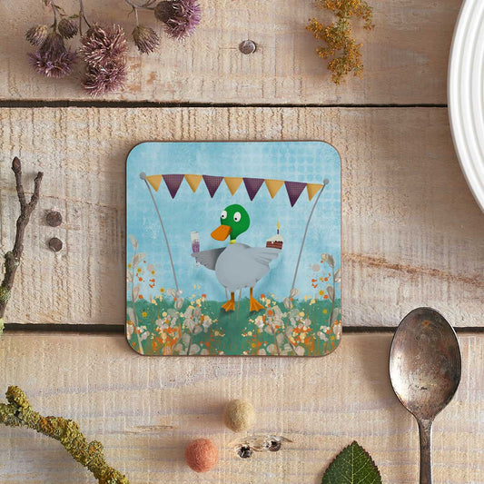 square coaster with an illustration of a duck holding a glass of champagne and a piece of cake