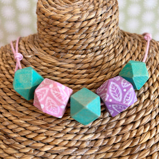 Faceted wooden beads with white leaf illustrations strung on pink cord