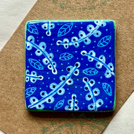 square ceramic brooch with blue background and white illustrated flowers and leaves