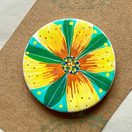 circular ceramic brooch with warm coloured flower illustration