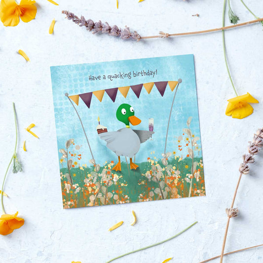 greeting card with a duck holding a glass of champagne and a cupcake